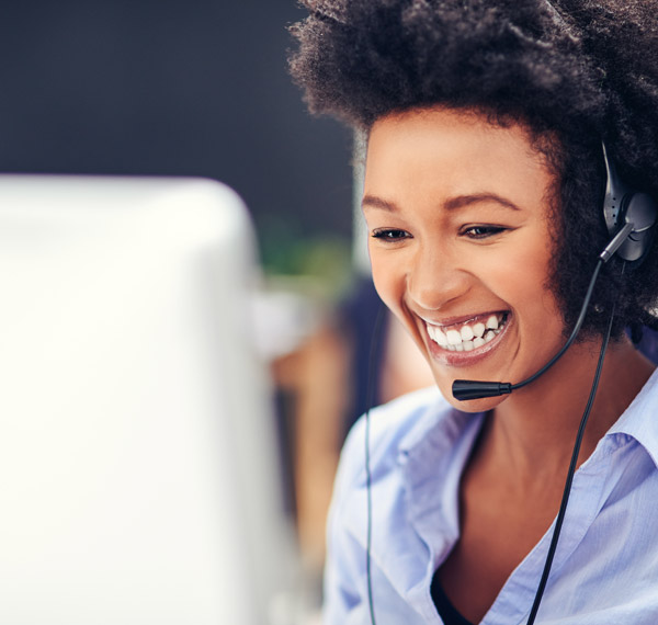 Smiling Customer Service worker with earphones in front of computer.